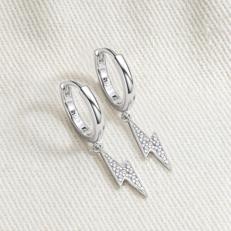 Silver hoop earrings with lightning bolt charms on a light fabric background